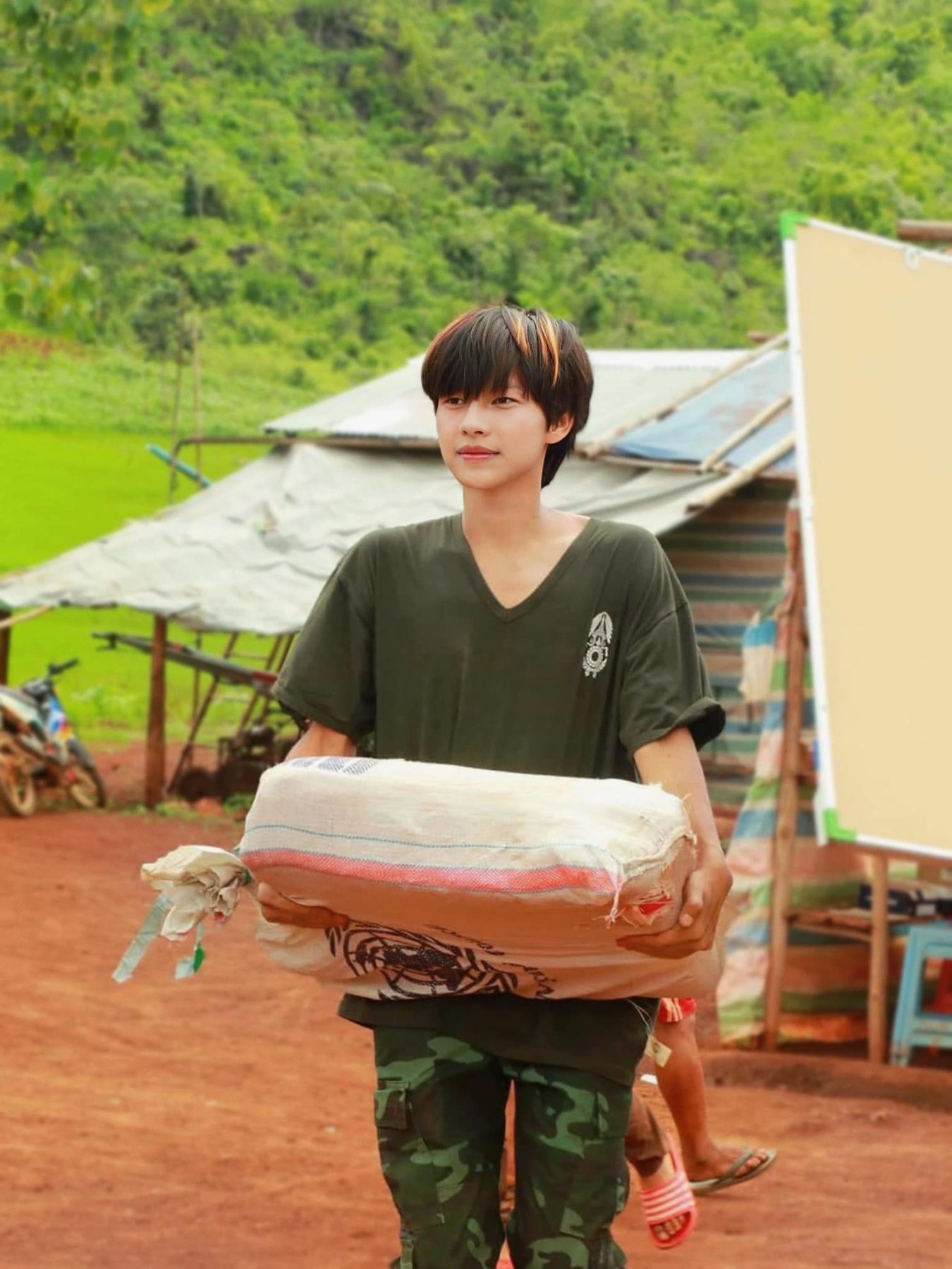 A volunteer in an olive shirt carries a large bundle of supplies along a dirt path.