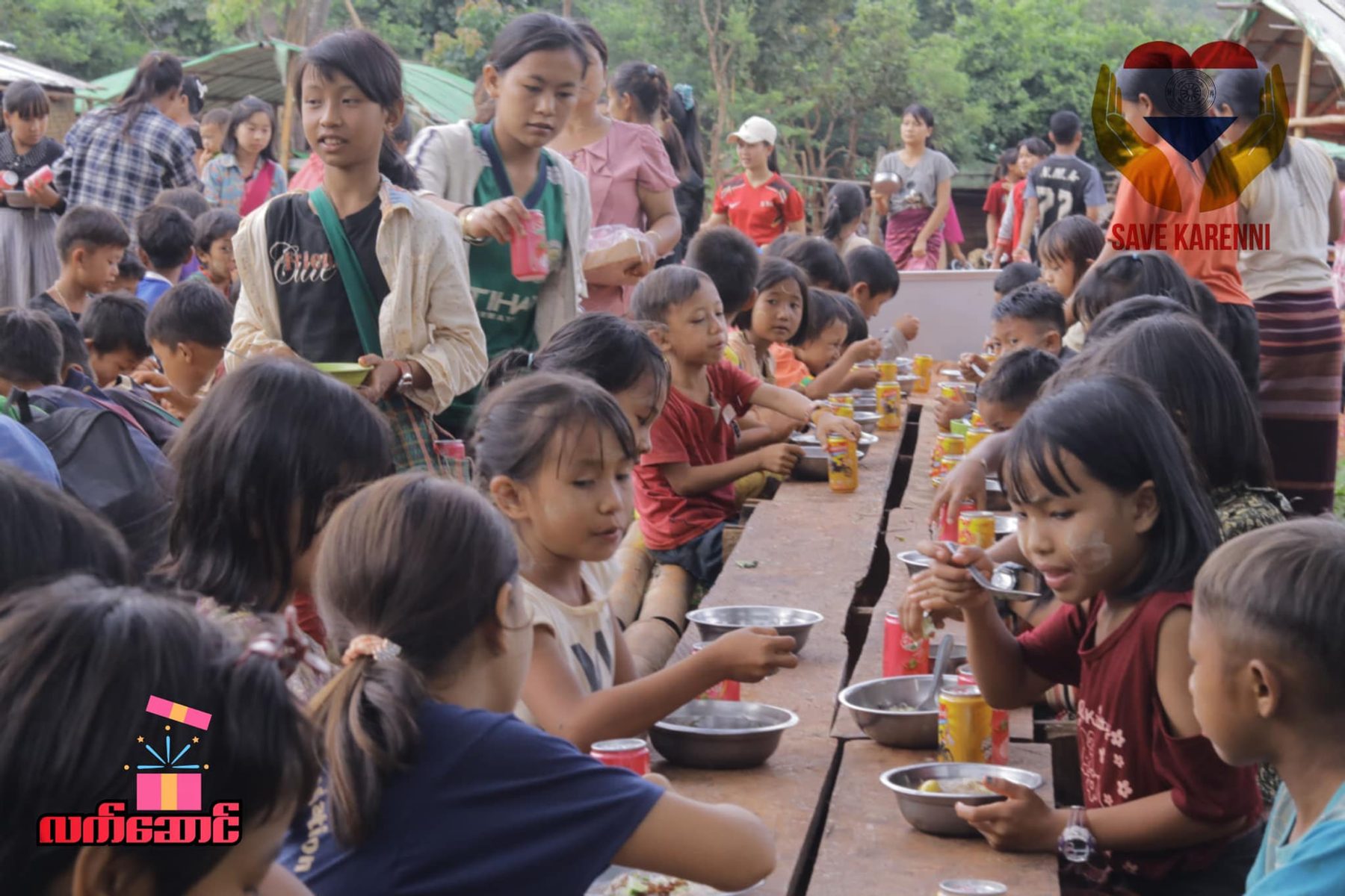 Children eat at long wooden tables under a canopy, with a Save Karenni logo in the corner.