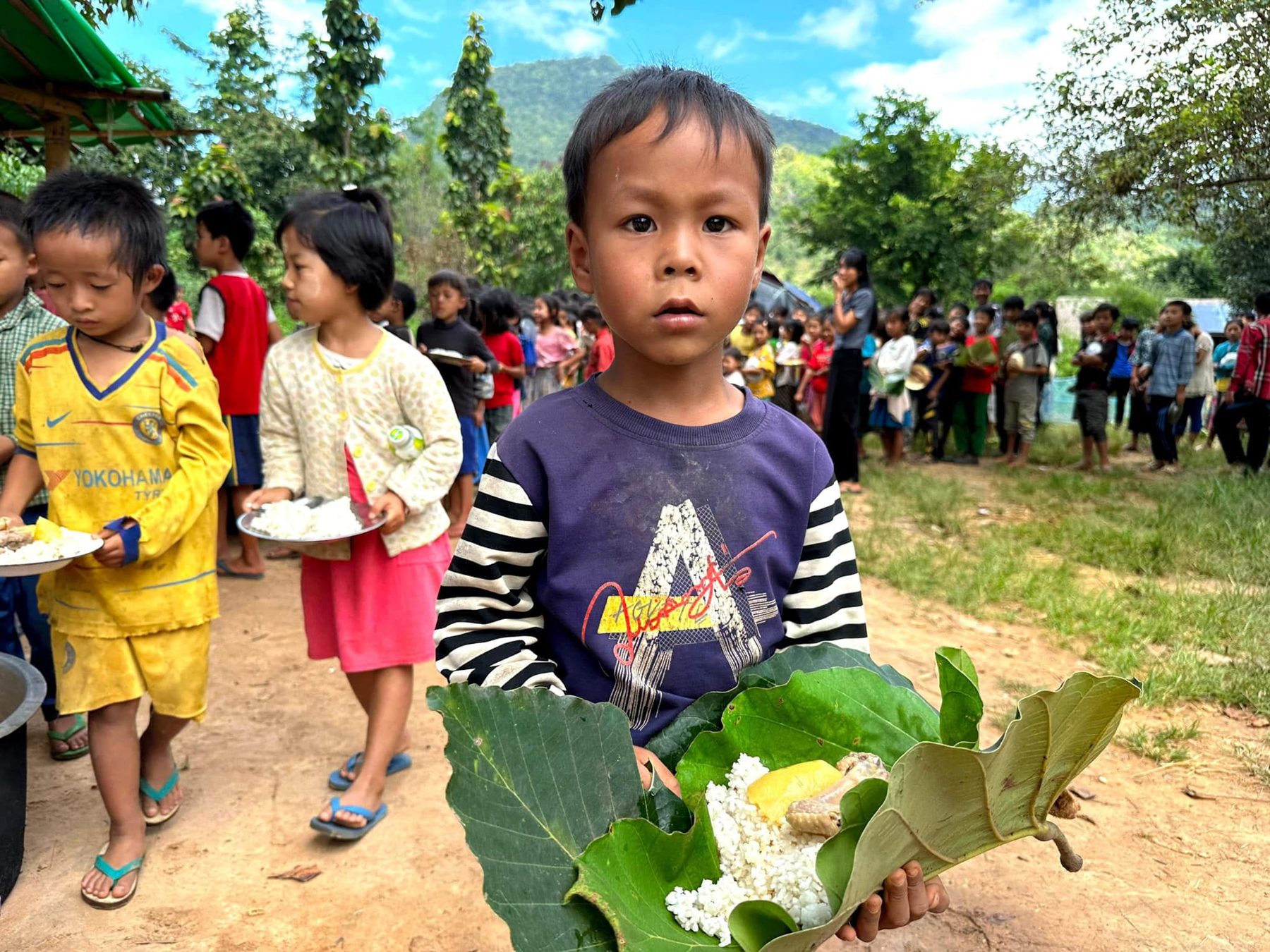 A boy holds rice served on a large green leaf, with other children behind him.