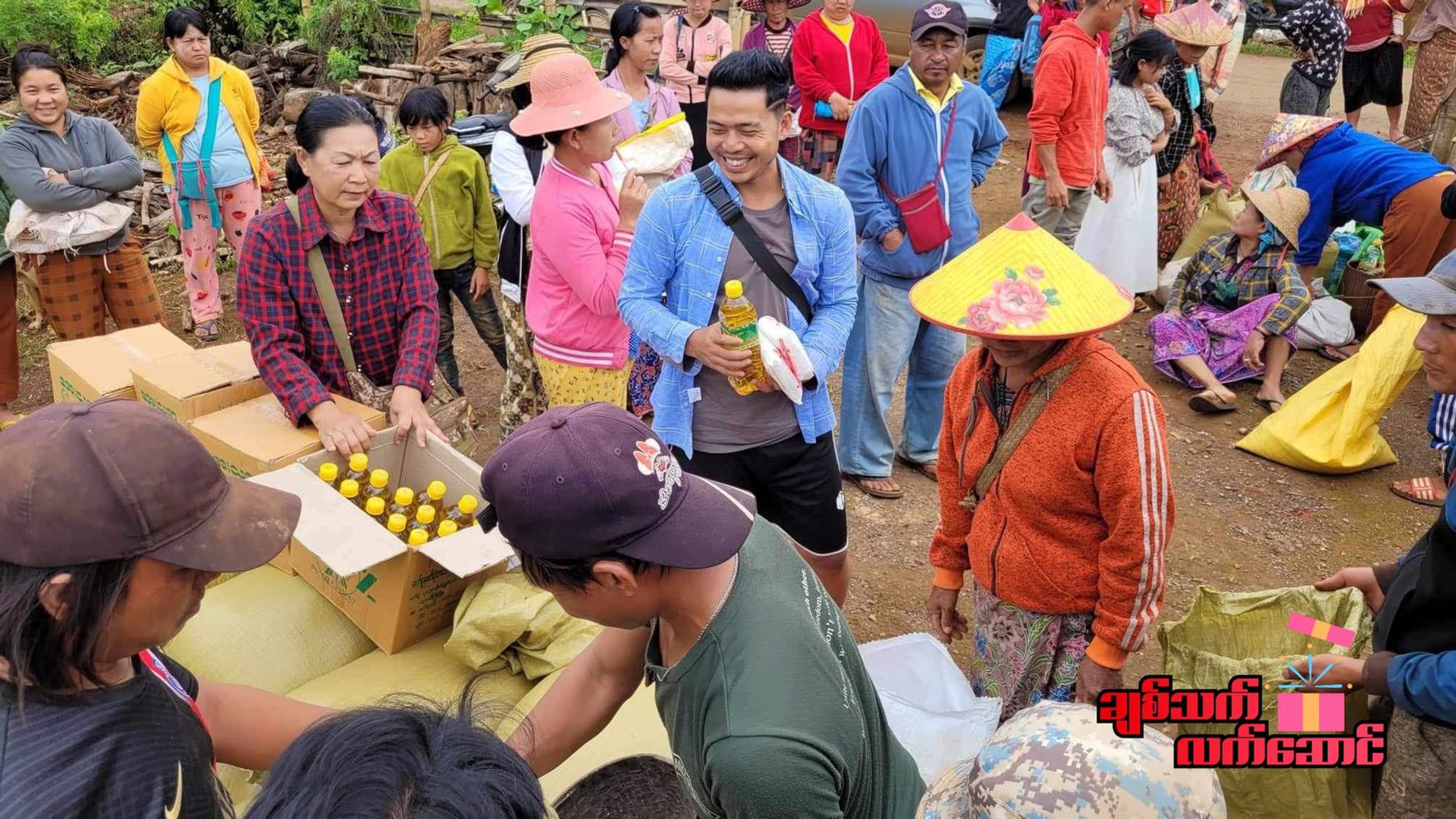 A crowd gathers around boxes of supplies being handed out outdoors.