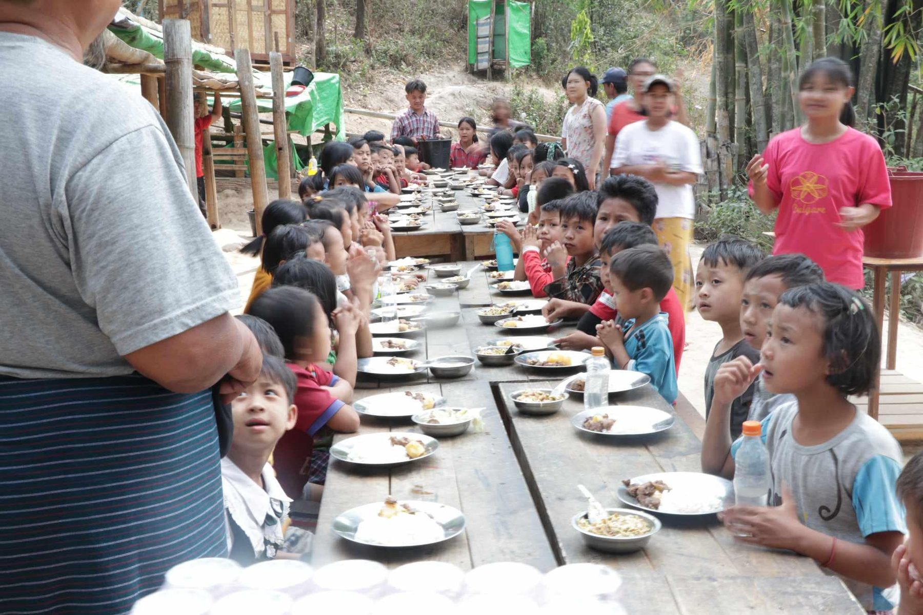 Children stand along a very long table set with plates.