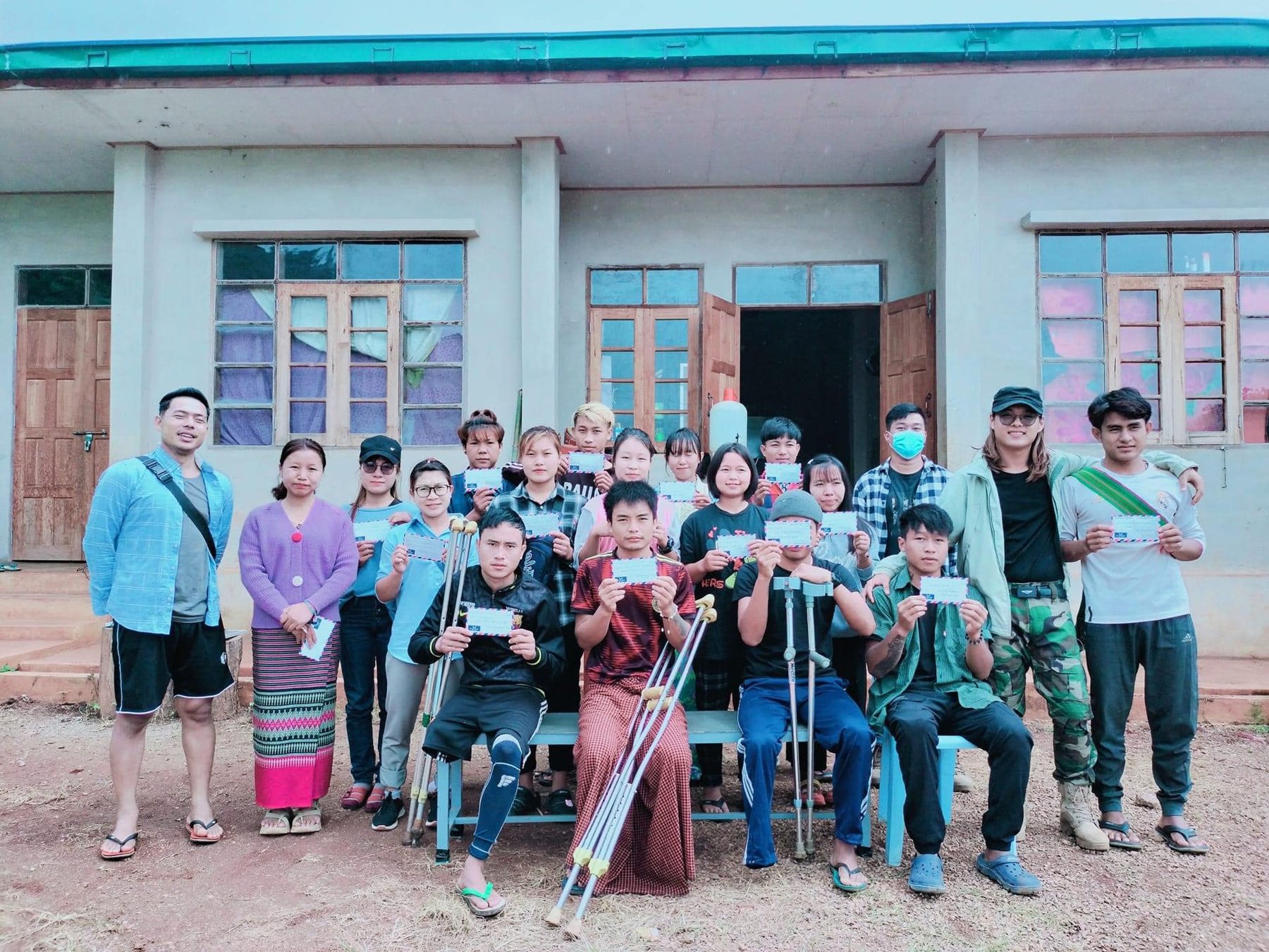 A group of people, some on crutches, pose in front of a pale blue school building.