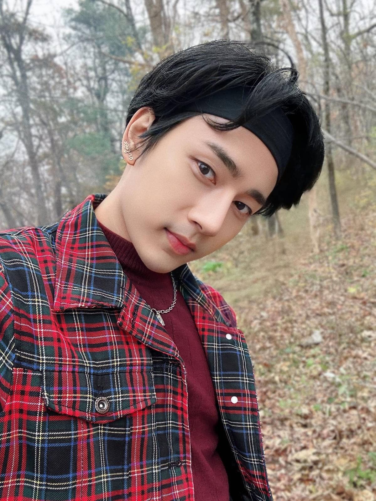 Wai Yan Aung in a red plaid jacket and a black headband, outdoors among bare autumn trees.