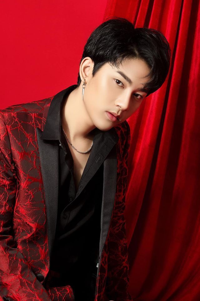 Wai Yan Aung in a patterned red jacket, standing in front of a red stage curtain.