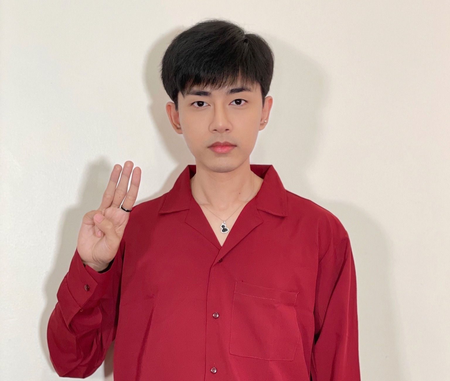 Wai Yan Aung in a red shirt raises the three-finger salute, against a white background.