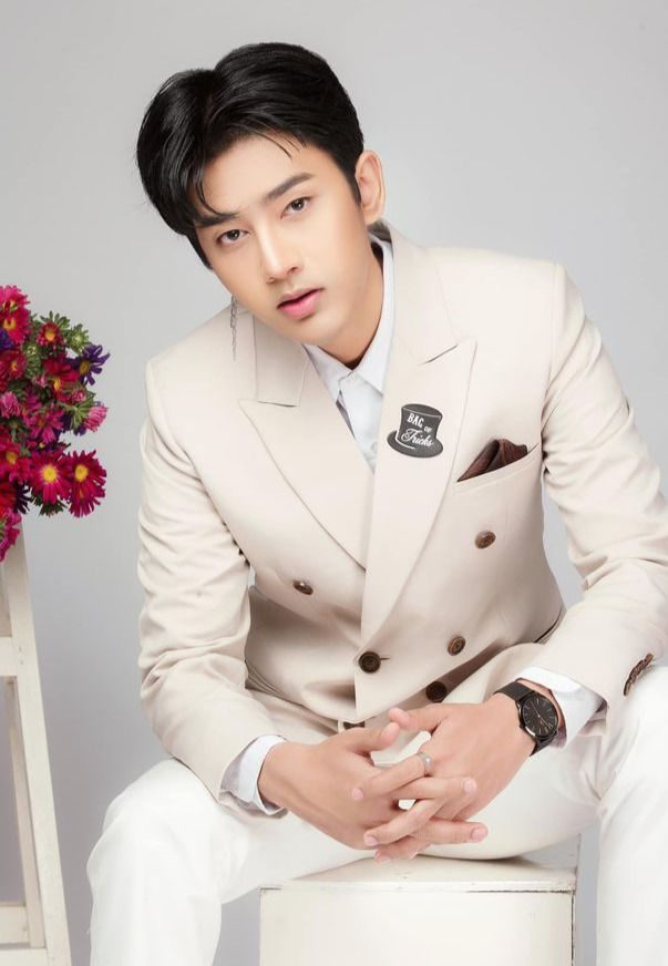 Wai Yan Aung seated in a cream double-breasted suit, with red flowers beside him.